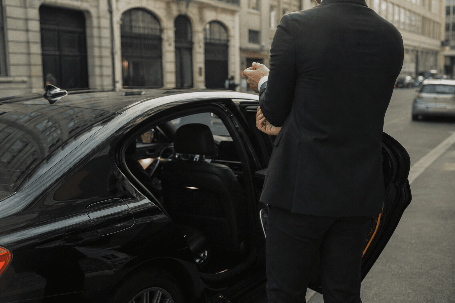 Chauffeur de dos ouvrant la portière d'une berline premium en attente dans une rue bruxelloise
