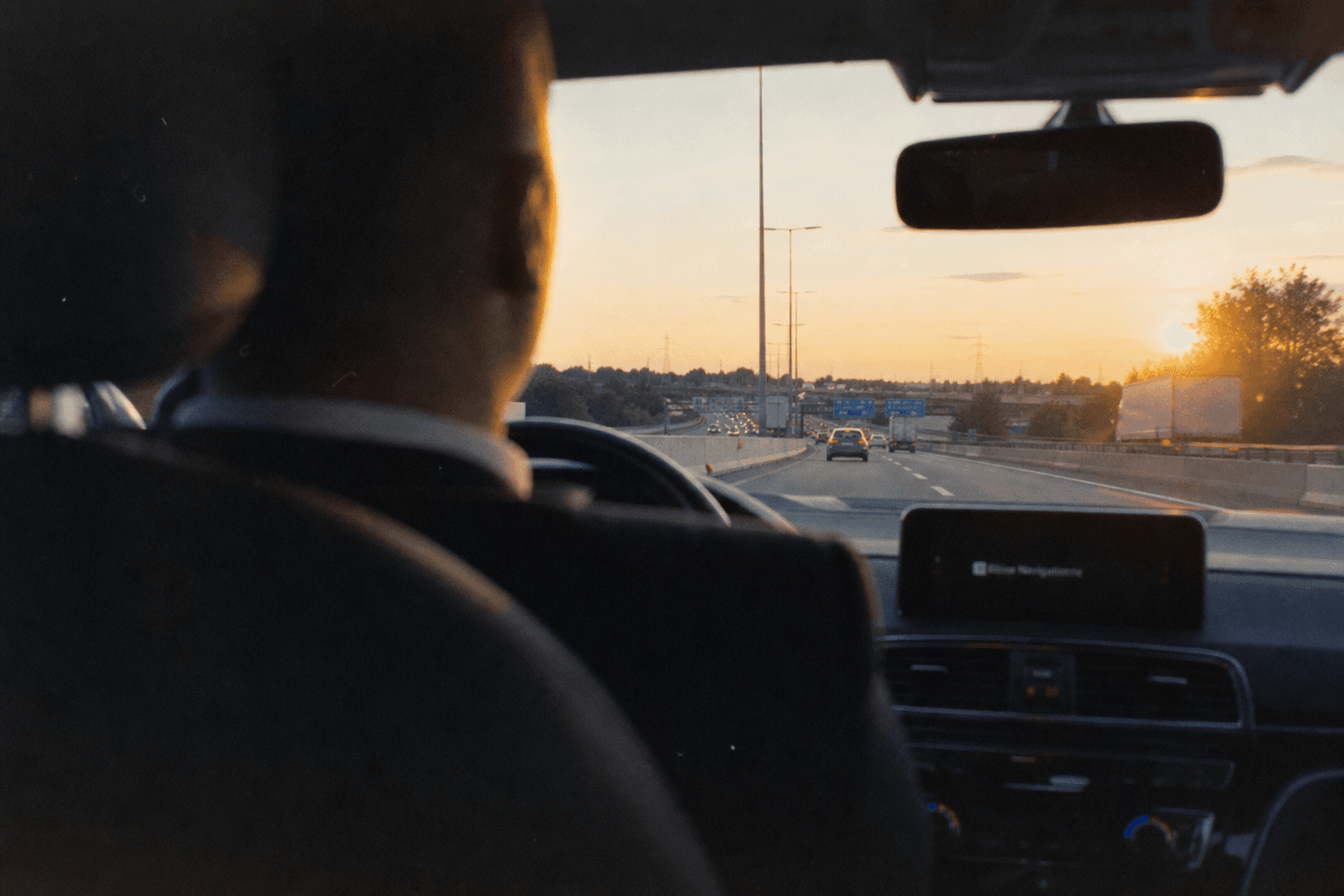 Vue depuis la banquette arrière vers l'autoroute au coucher du soleil, nuque du chauffeur en amorce